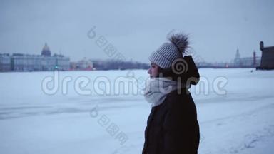 穿着温<strong>暖</strong>夹克和帽子的年轻女孩在寒冷中。 年轻的女人在雪堆和雪城的背景下。 <strong>冬季</strong>